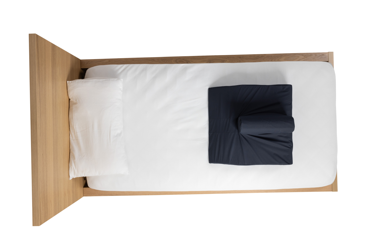 Aerial of a black CareWave FiTLeG leg positioning cushion on a wooden bed in a supine configuration.