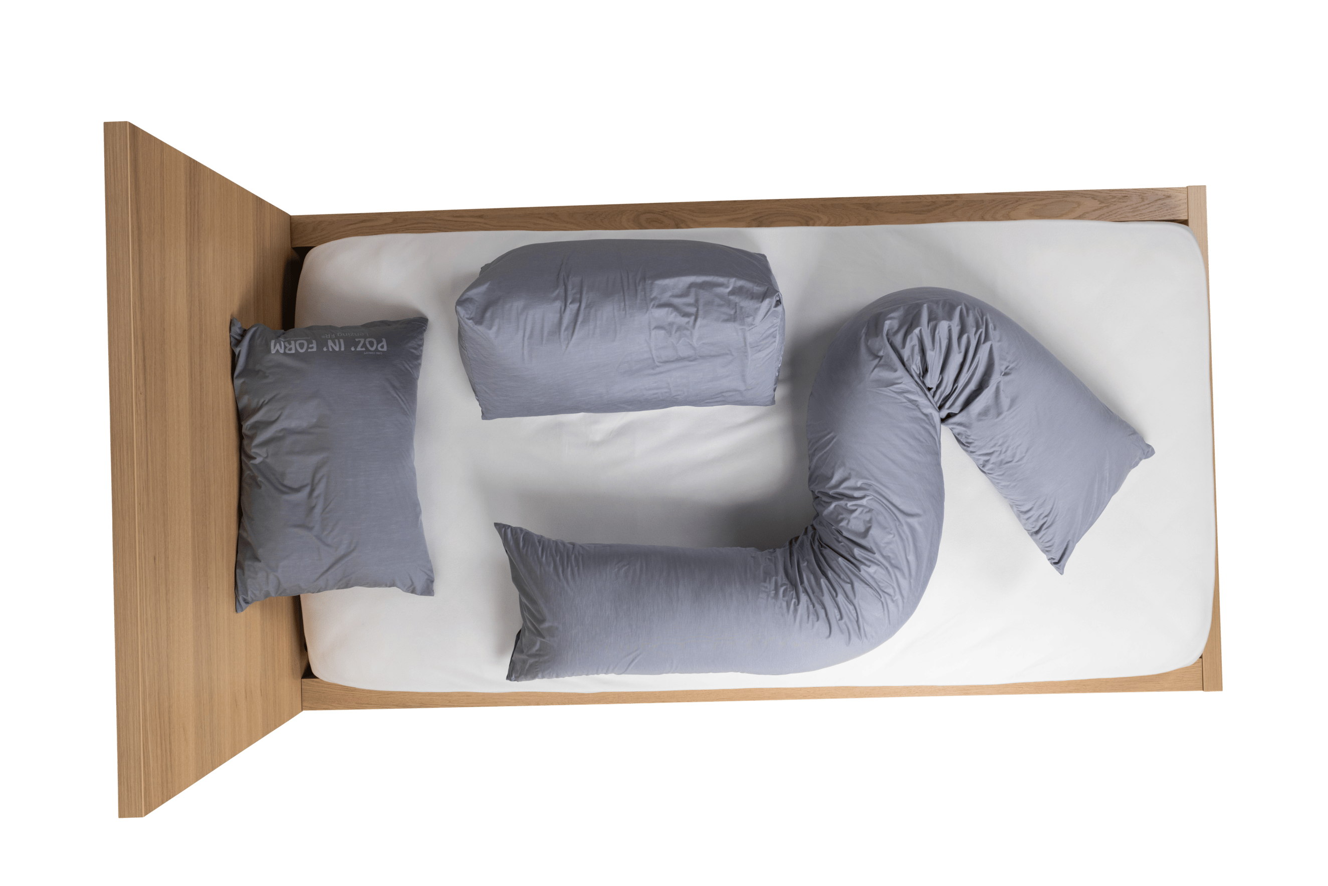 Aerial view of grey Poz'In'Form postural positioning cushions - specifically a universal cushion at the head of the bed, followed by a delta wedge cushion and a decubitus cushion - lying on a white mattress on a wooden bed.