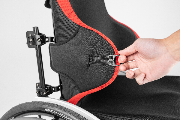 Manta Back support lateral support attached to manual wheelchair. Hand is pulling the swing away lateral tab to allow for seamless transfers