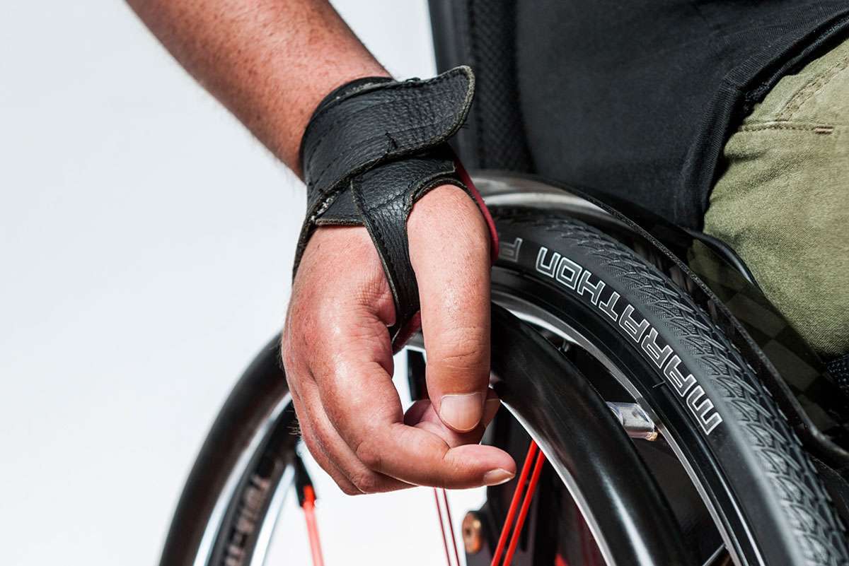 Close up image of a hand pushing a wheelchair with hand glove.