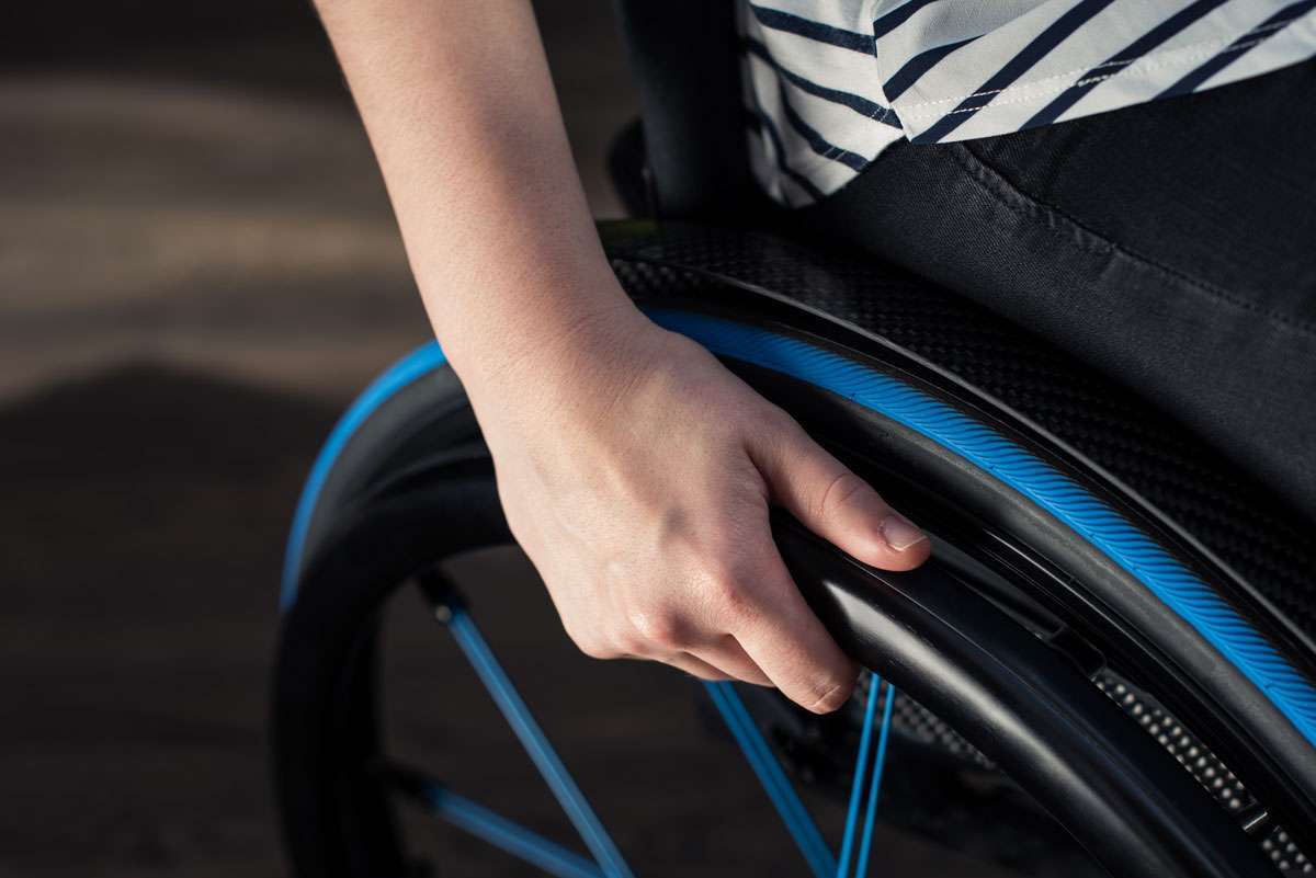 Close up image of a hand holding onto a wheelchair rim with blue spokes and rim