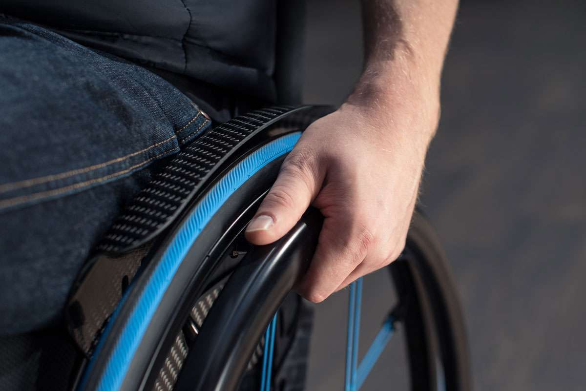 Close up image of a hand holding onto a wheelchair rim with blue spokes and rim from the front.