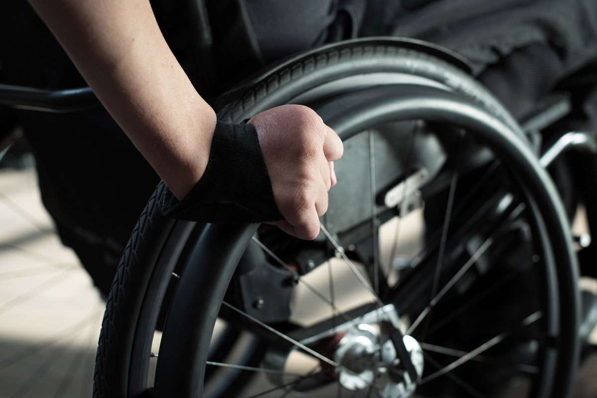 Close up image of the back of a hand pushing a wheelchair rim with a gloved on.