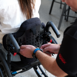 A man wearing a Spex uniform adjusts a wheelchair back support whilst the client sits in the wheelchair.