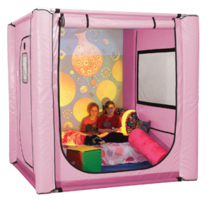 Two young girls sitting on a mattress with cushions and lights inside a pink SafeSpace tent.