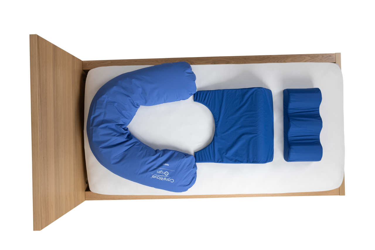 Aerial view of a blue CareWave half-moon cushion and a blue CareWave FiTLeG non-slip leg positioning cushion on a wooden bed.