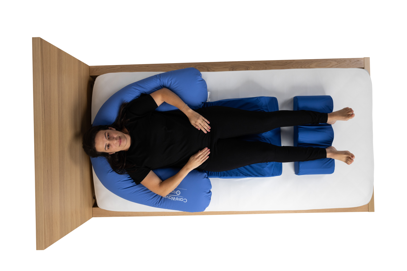 Aerial view of a blue CareWave half-moon cushion and a blue CareWave FiTLeG non-slip leg positioning cushion with user on a wooden bed.