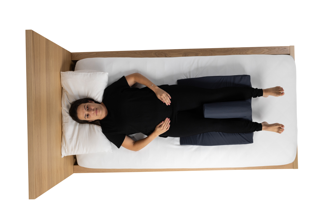 Aerial view of a black CareWave Evo FiTLeG leg positioning cushion on a wooden bed in a supine configuration with user.