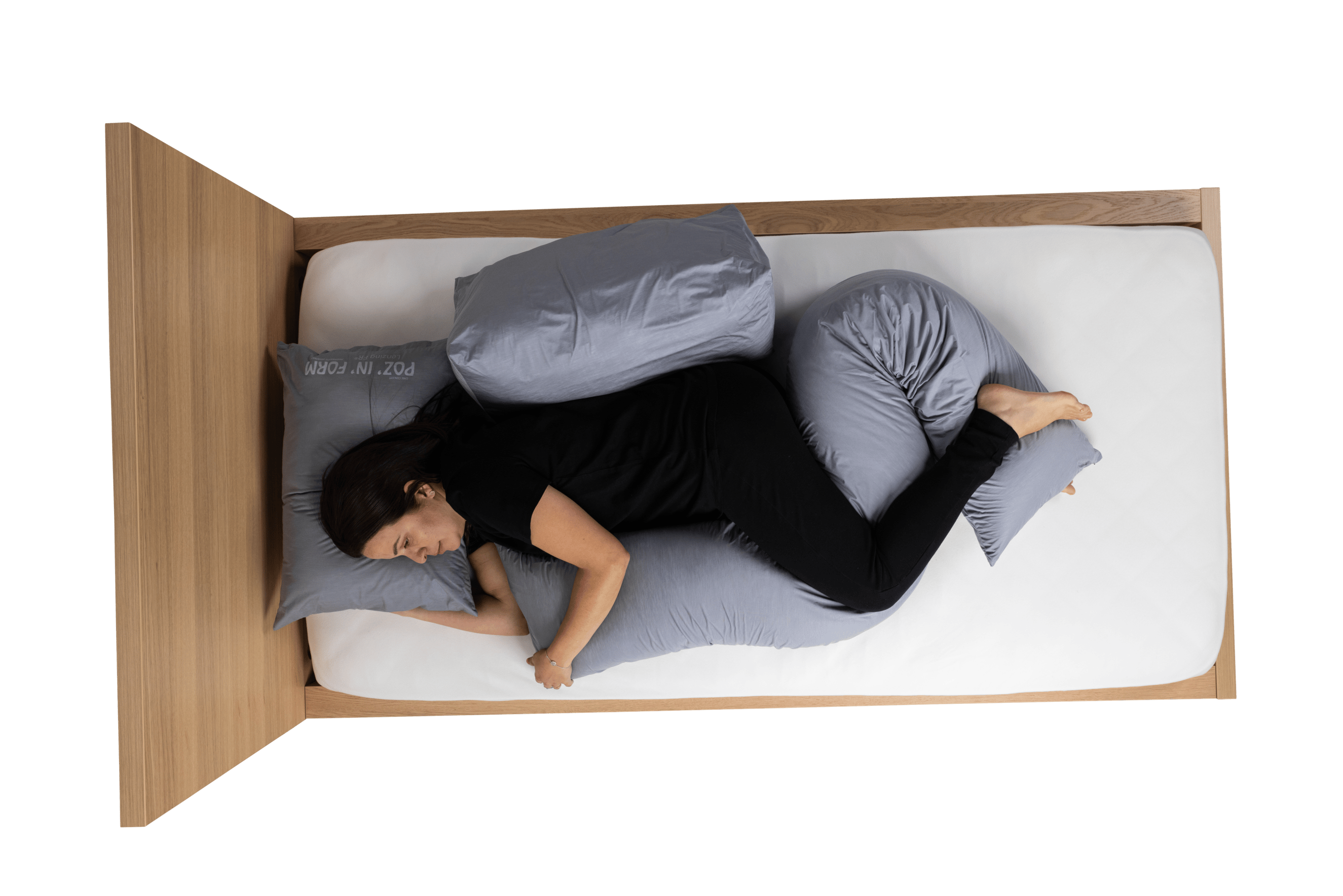 A Birds-eye image of a lady dressed in black on a bed on a white background, with a Universal, Delta and Decubitus sleep positioning cushion.