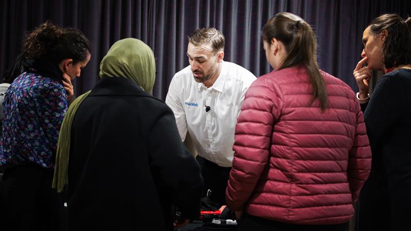 Man in white shirt leaning over a table as a group watch.