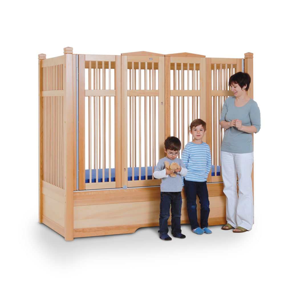 A mother and her two young sons stand by a Safe Surround Plus Bed with high timber sides and blue mattress for safety and stability.