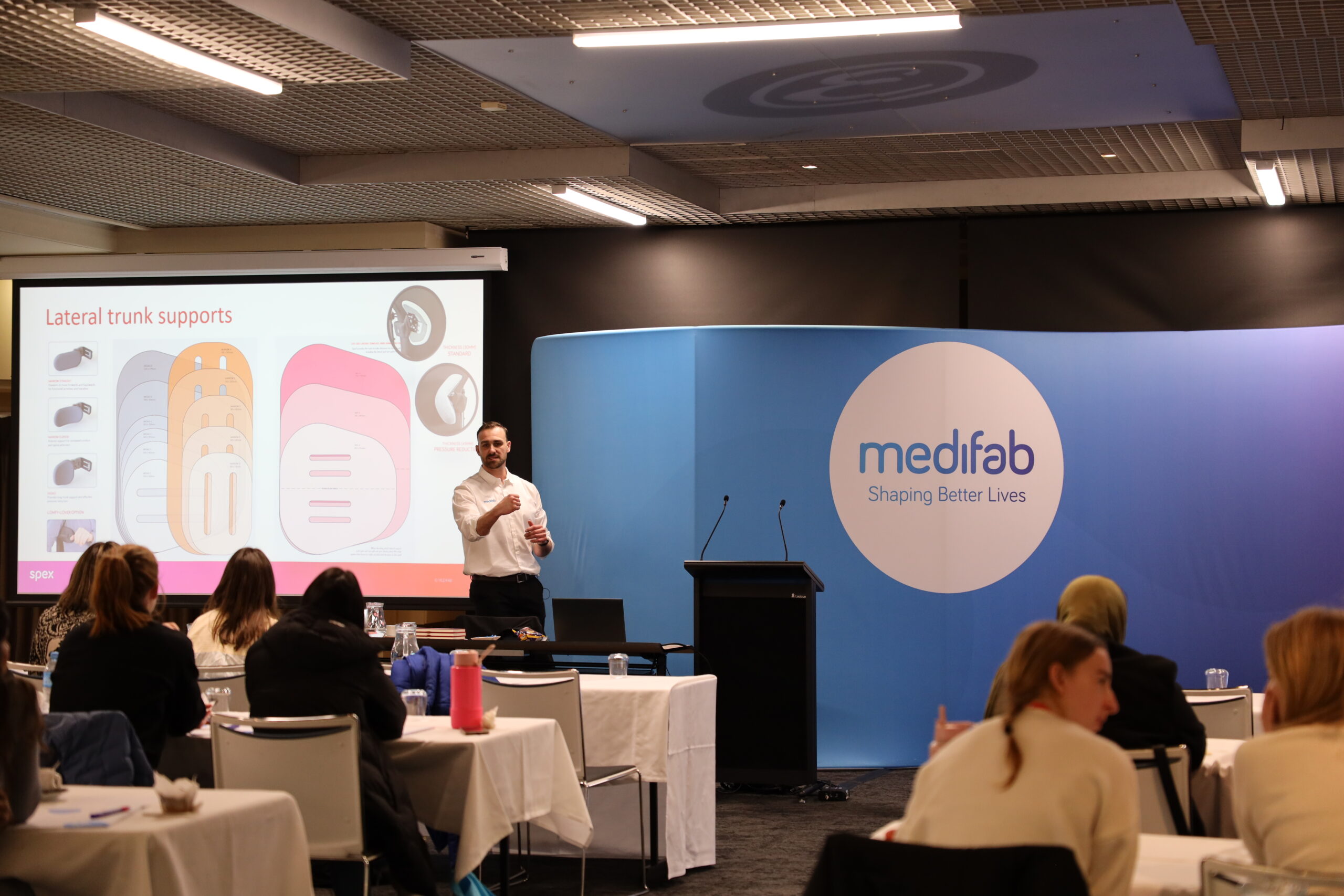 Room of therapists listening to a man in a white Medifab shirt